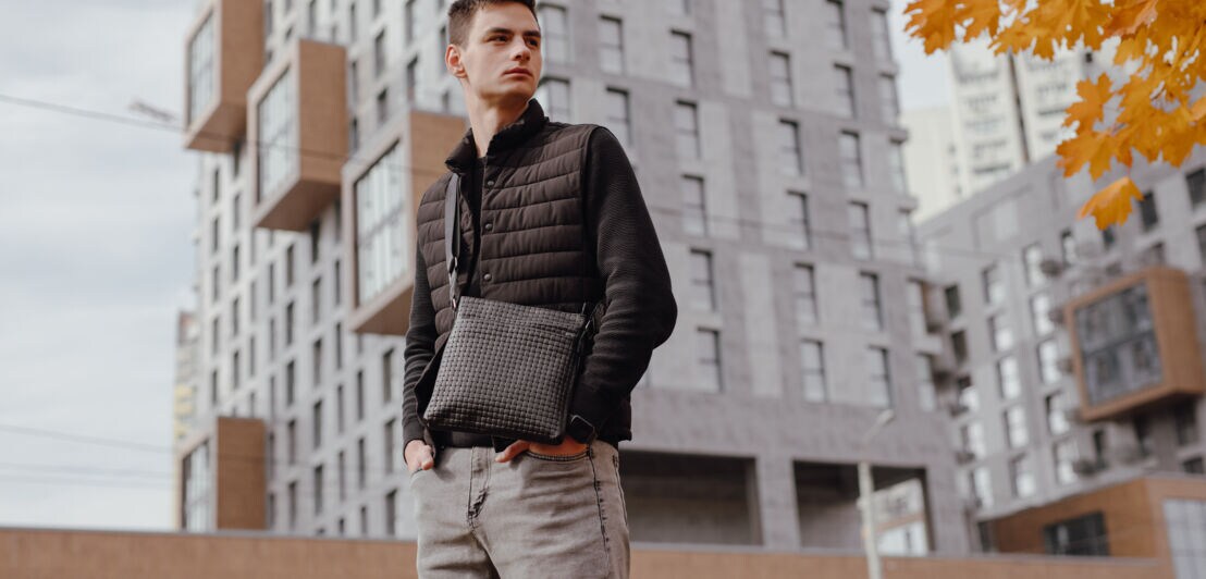 Fashion man holding black messenger bag in the autumn city