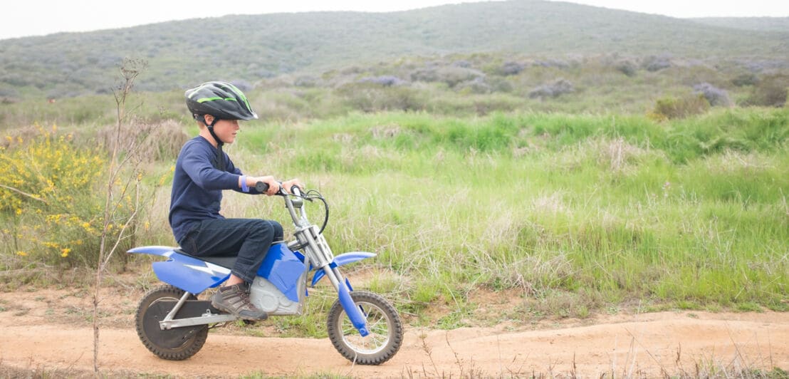 Ein Junge fährt ein Elektro-Kindermotorrad auf einem Feldweg.