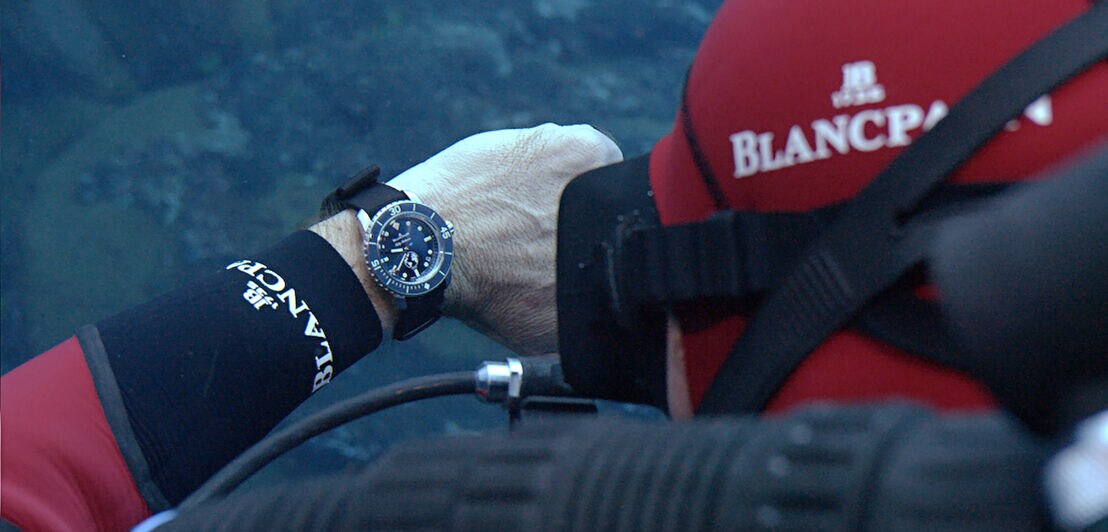 Ein Taucher schaut unter Wasser auf seine Taucheruhr von Blancpain. 