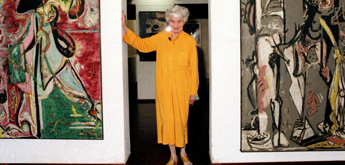 Porträt von Peggy Guggenheim in einem gelben Kleid zwischen zwei abstrakten Gemälden