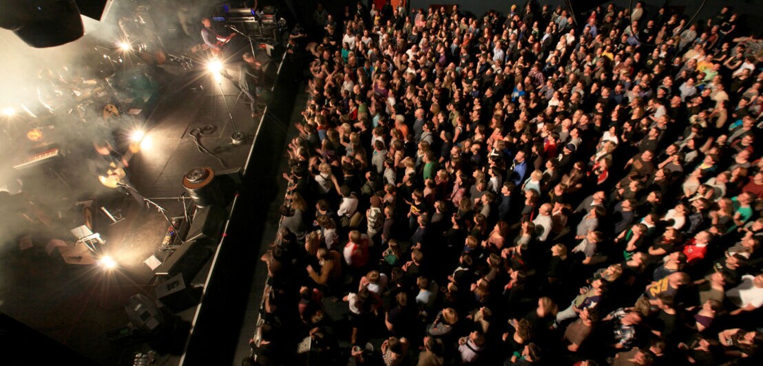 Eine Band spielt auf einer Bühne vor Publikum in einer Konzerthalle, Aufnahme aus der Vogelperspektive