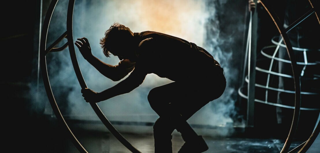 Silhouette eines Artisten in einem Reifen auf einer Bühne vor künstlichem Nebel