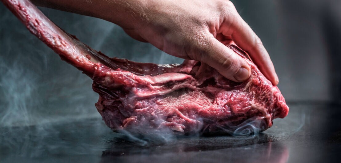 Eine Hand drückt ein Stück Fleisch auf eine Platte; es entsteht Dampf.
