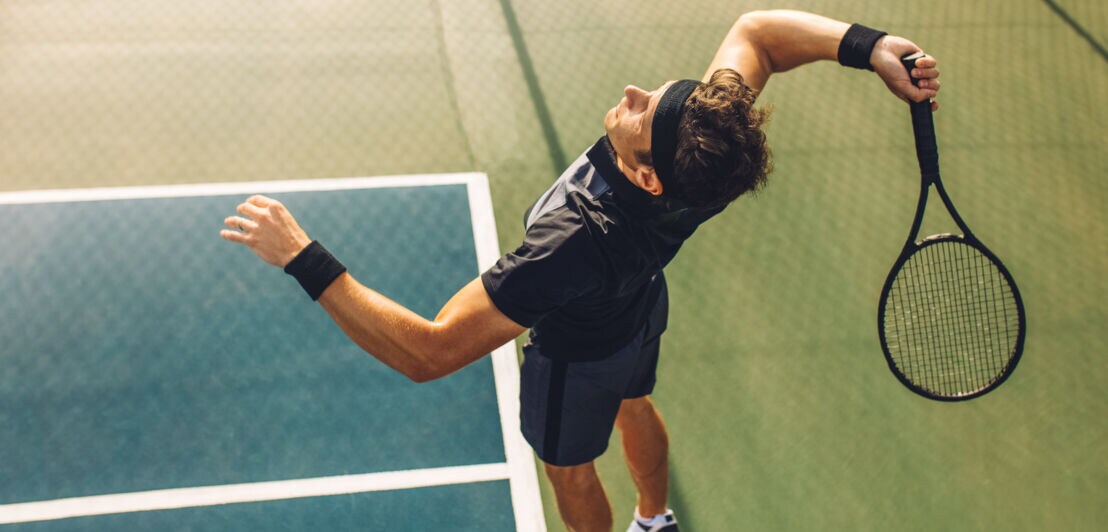Ein Tennisspieler schwingt den Schläger zum Aufschlag.