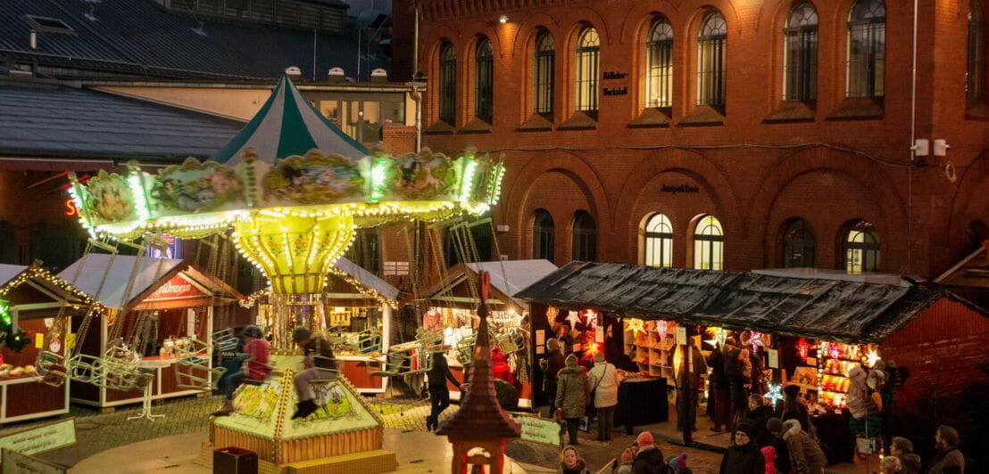 Kettenkarussel und Weihnachtsmarktbuden vor der Kulturbrauerei in Berlin.