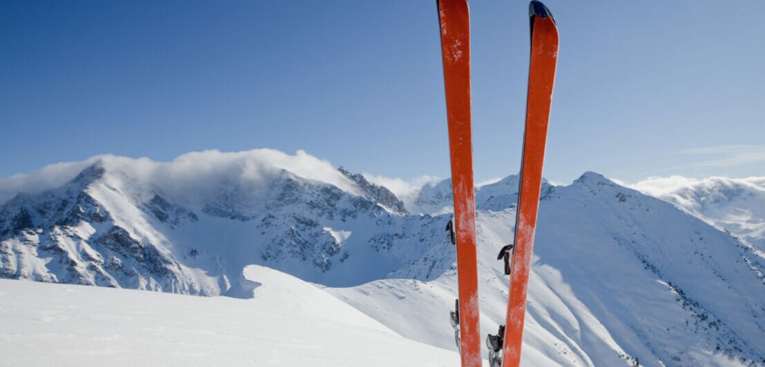 Ein Paar Ski steckt senkrecht im Schnee vor Bergpanorama