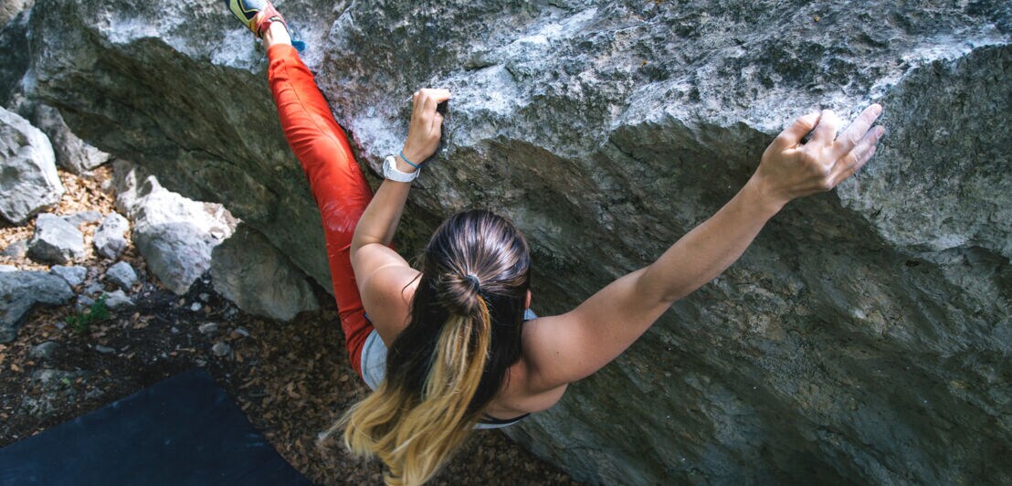 Blick von oben auf eine Person mit langen Haaren, die an einer Felswand bouldert