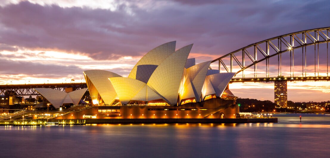 Beleuchtetes Sydney Opera House mit Harbour Bridge in der Abenddämmerung