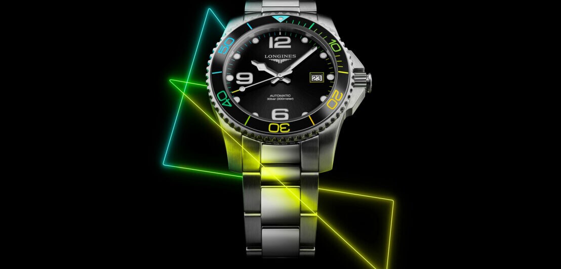 Uhr aus Metall auf dunklem Hintergrund, um die sich neonfarbene Muster winden