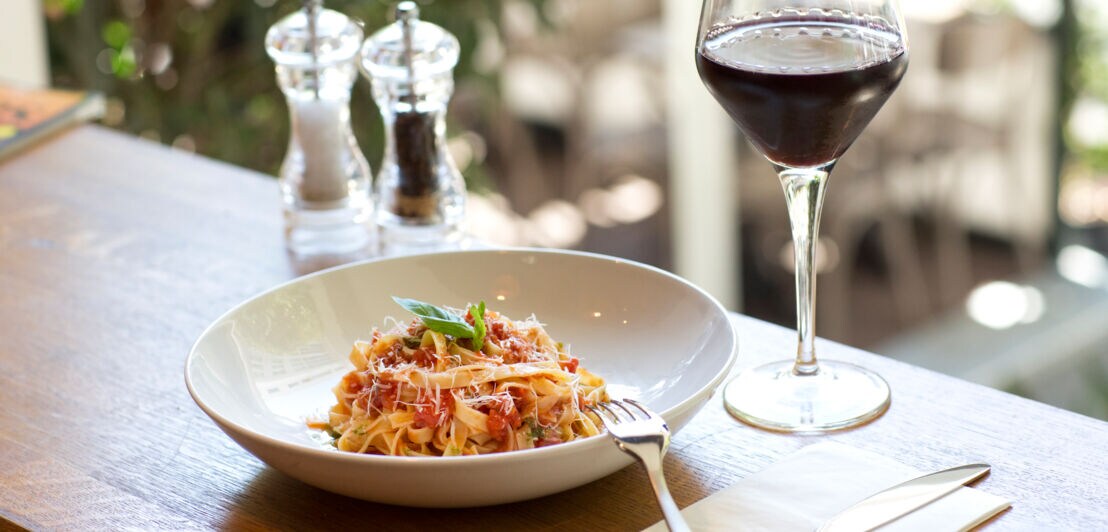 Ein Teller Pasta mit roter Sauce, daneben ein Glas Rotwein sowie Salz- und Pfefferstreuer.