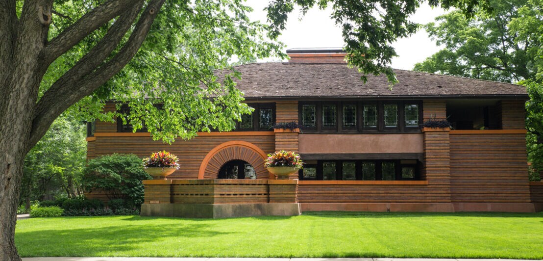 Ein braunes Steinhaus, entworfen von Frank Lloyd Wright, umrahmt von großen Bäumen