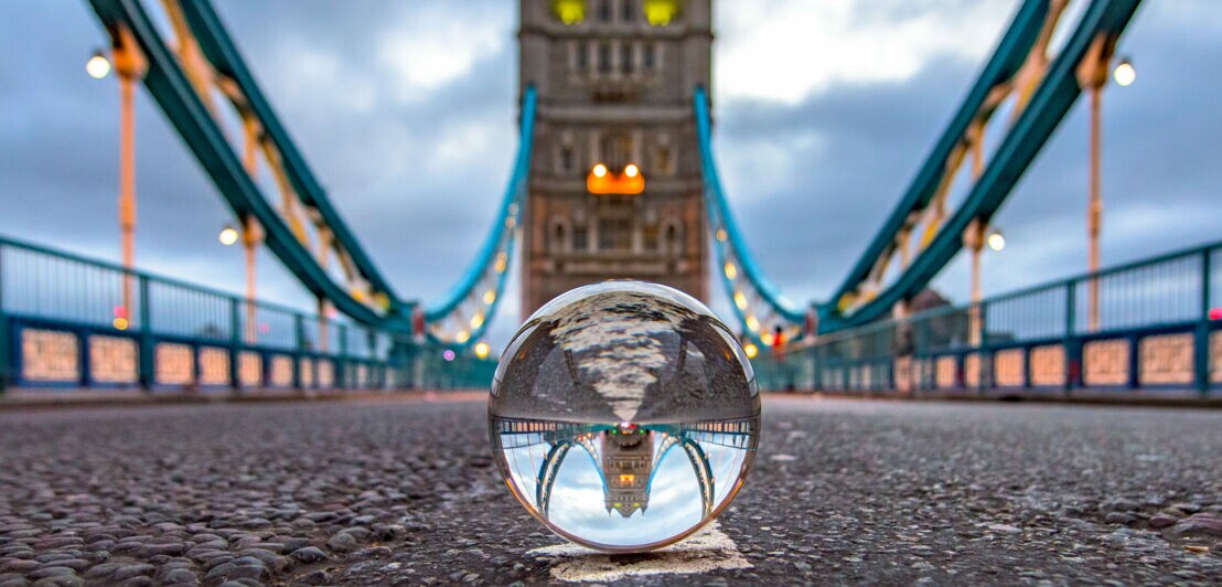 Die London Tower Bridge, die sich in einer Glaskugel spiegelt und selbst unscharf im Hintergrund zu sehen ist