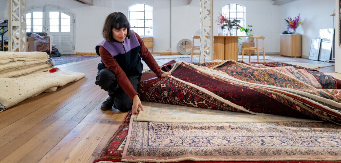 Anna Wahdat durchsucht einen Stapel mit rötlichen Orientteppichen