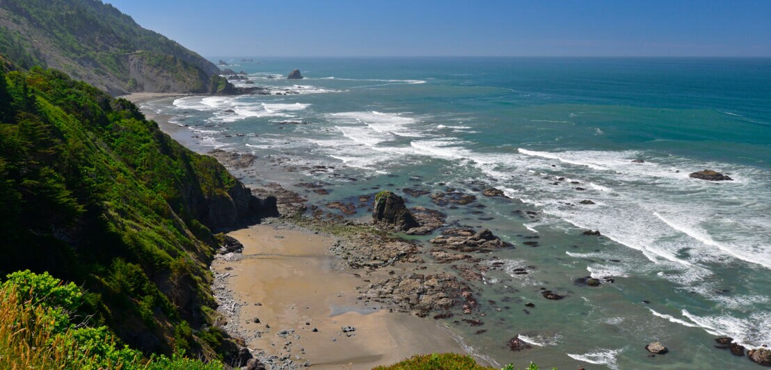 Panorama einer begrünten, gebirgigen Küste mit Felsen im Wasser