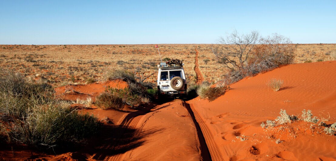 Ein Jeep, der durch eine rote Sanddünenwüste fährt