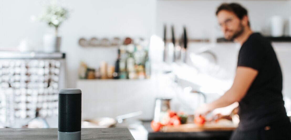 Foto einer Person, die in einer Küche steht und in Richtung einer Lautsprecherbox blickt