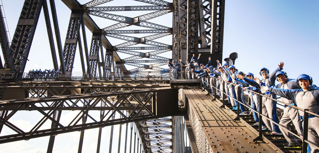 Männer und Frauen besteigen Sydneys Harbour Bridge und winken in die Kamera
