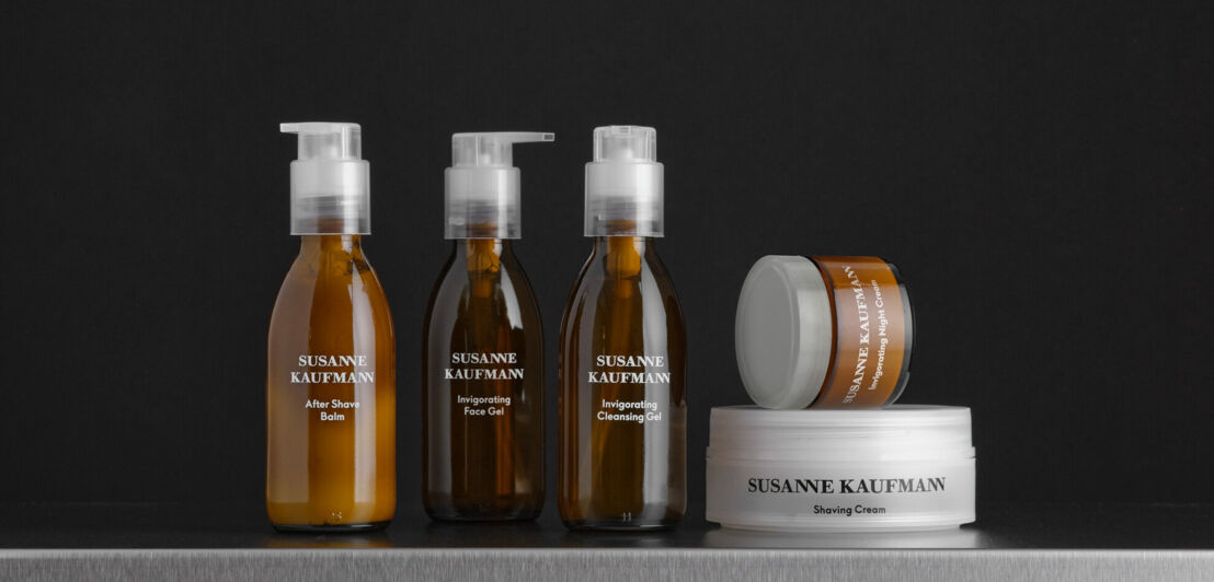 Drei Kosmetikflaschen und zwei Tiegel vor schwarzem Hintergrund, die Rasurprodukte von Susanne Kaufmann enthalten