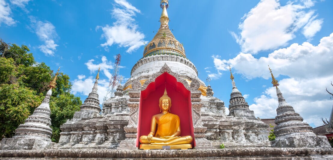 Tempel mit goldener Buddhastatue vor rotem Hintergrund