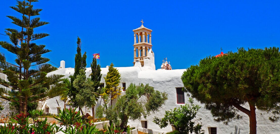 Das Kloster Panagia Tourliani auf Mykonos, davor ein Garten mit Büschen und Bäumen
