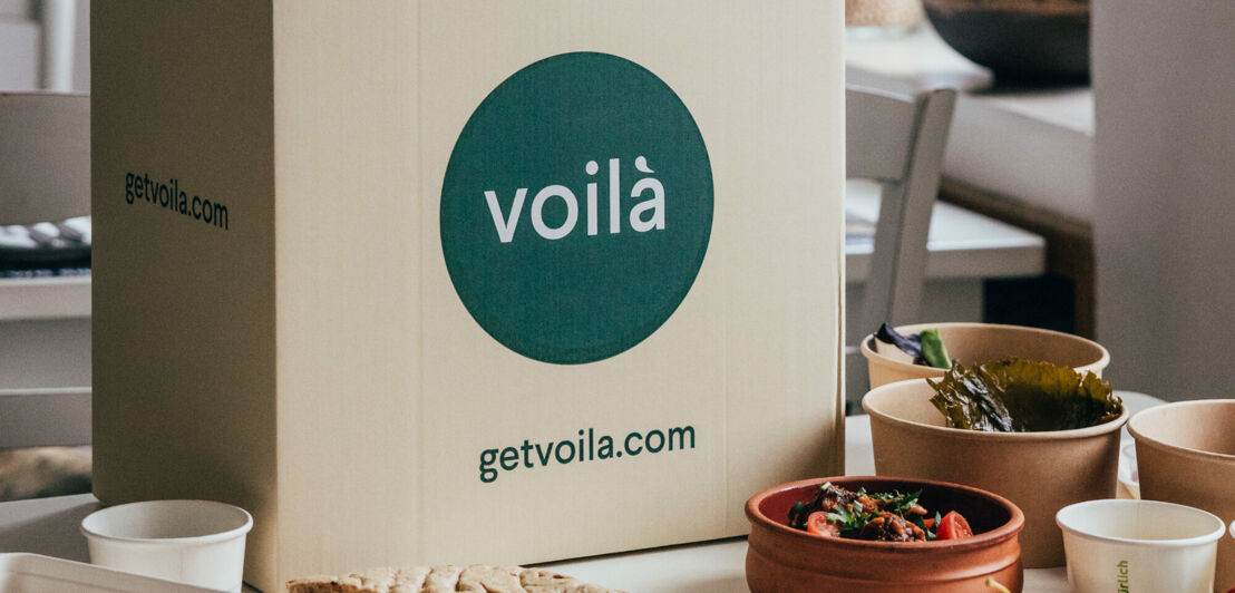 Kochbox von Voilà auf einem Tisch, eingerahmt von Schalen mit Zutaten