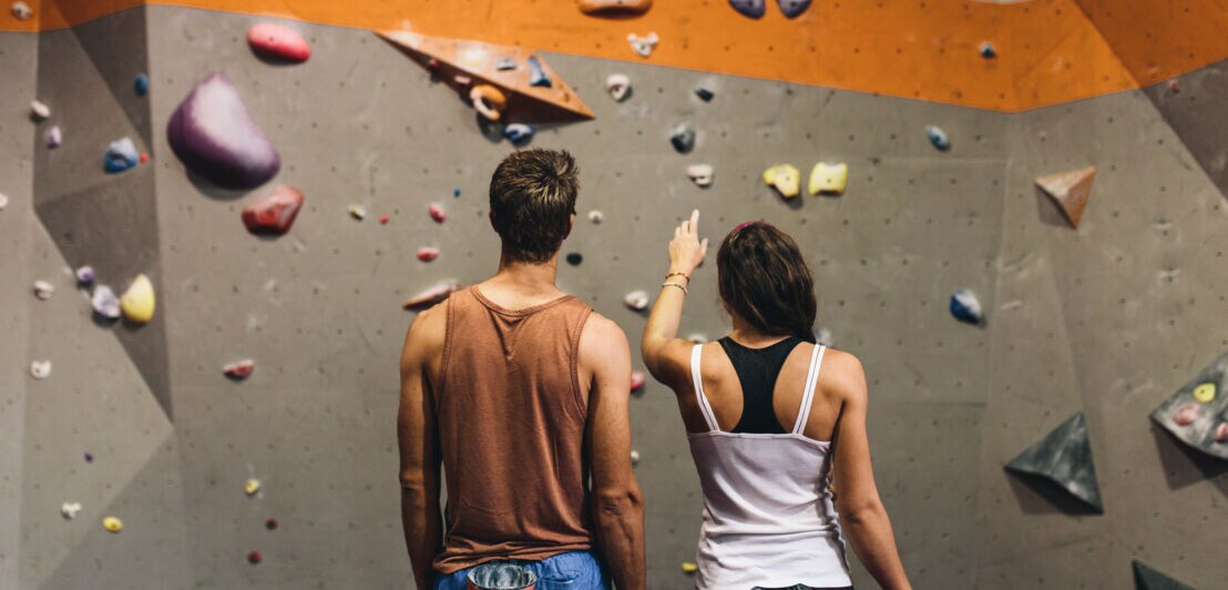 Zwei Personen in Sportkleidung stehen vor einer Kletterwand
