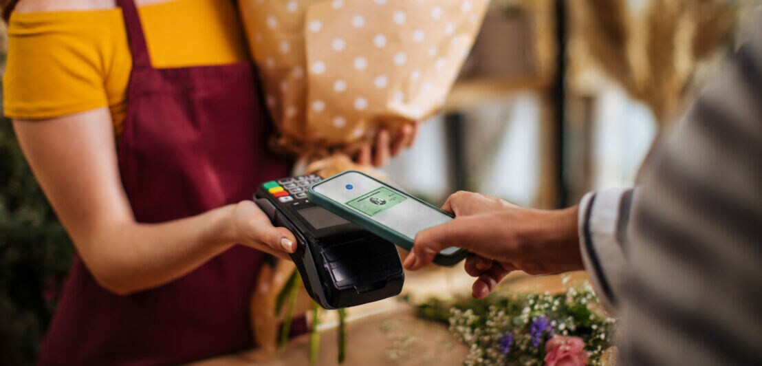 Ein Kunde zahlt in einer Amex Akzeptanzstelle kontaktlos mit Kreditkarte per Apple Pay mit dem Smartphone