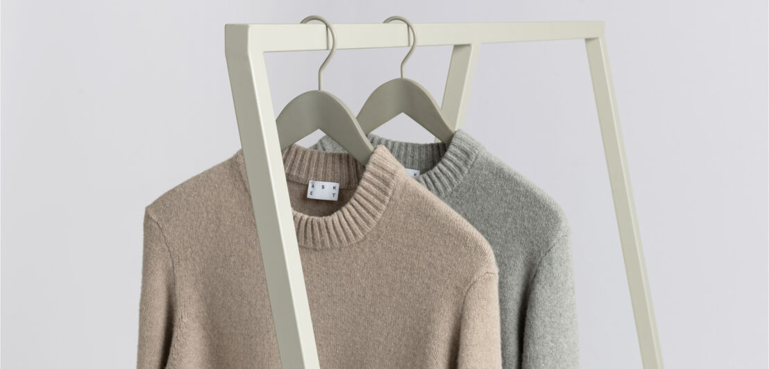 Zwei Pullover in Grau und Beige, die an einer Kleiderstange hängen