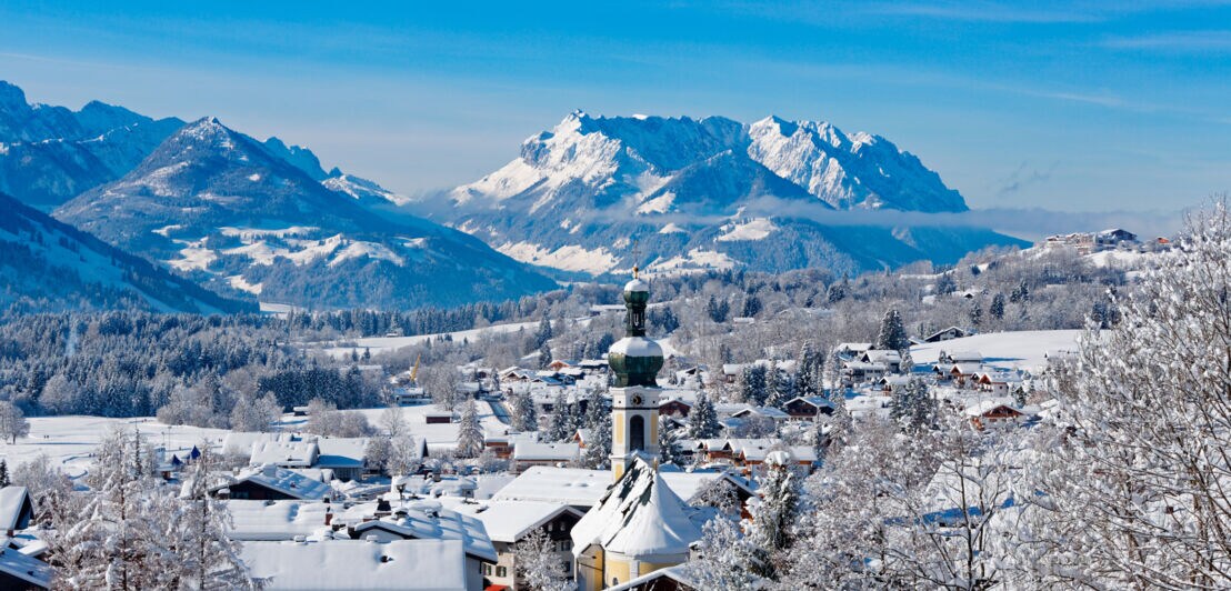 Verschneite Ortschaft mit Kirchturm vor Bergpanorama
