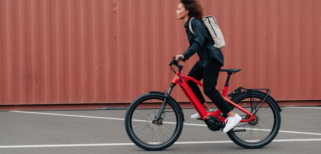 Eine Frau fährt auf einem roten E-Bike vor einem braunen Container