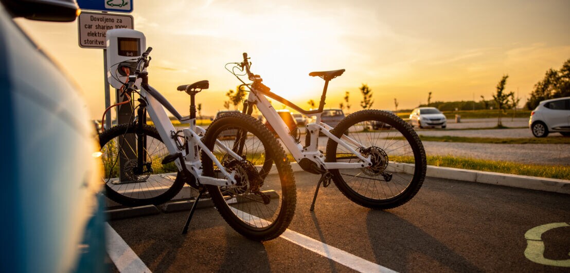 Zwei Elektrofahrräder werden während des Sonnenuntergangs an der Ladestation für Elektrofahrzeuge auf dem Parkplatz geladen