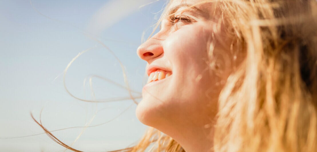 Nahaufnahme einer jungen Frau, die vor blauem Himmel in Richtung Sonne lacht