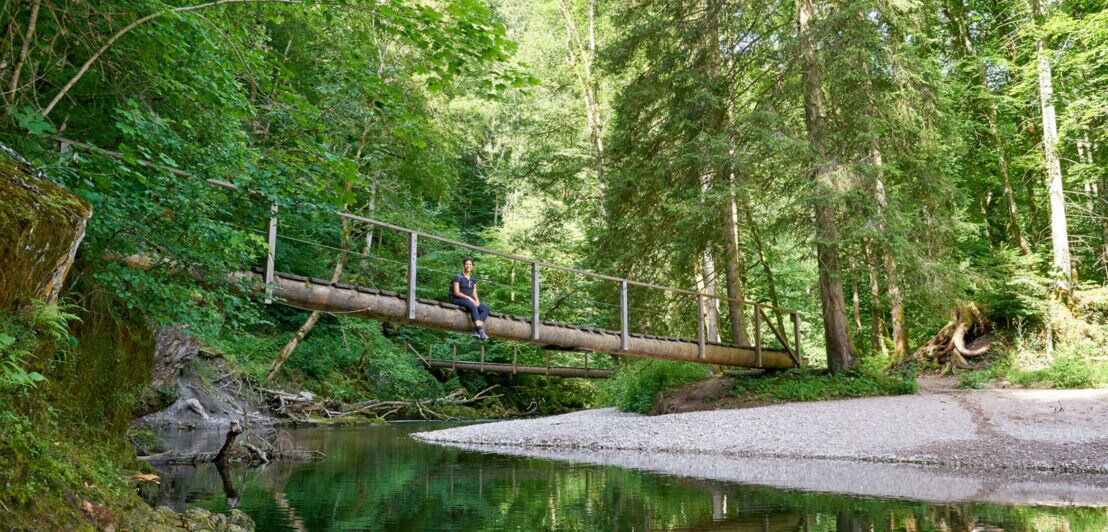 Eine Person sitzt auf einer Holzbrücke über einem Fluss
