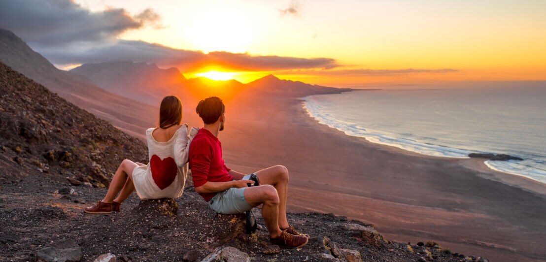 Zwei Menschen blicken bei ihrer Wanderung auf Fuerteventura aufs Meer bei Sonnenuntergang