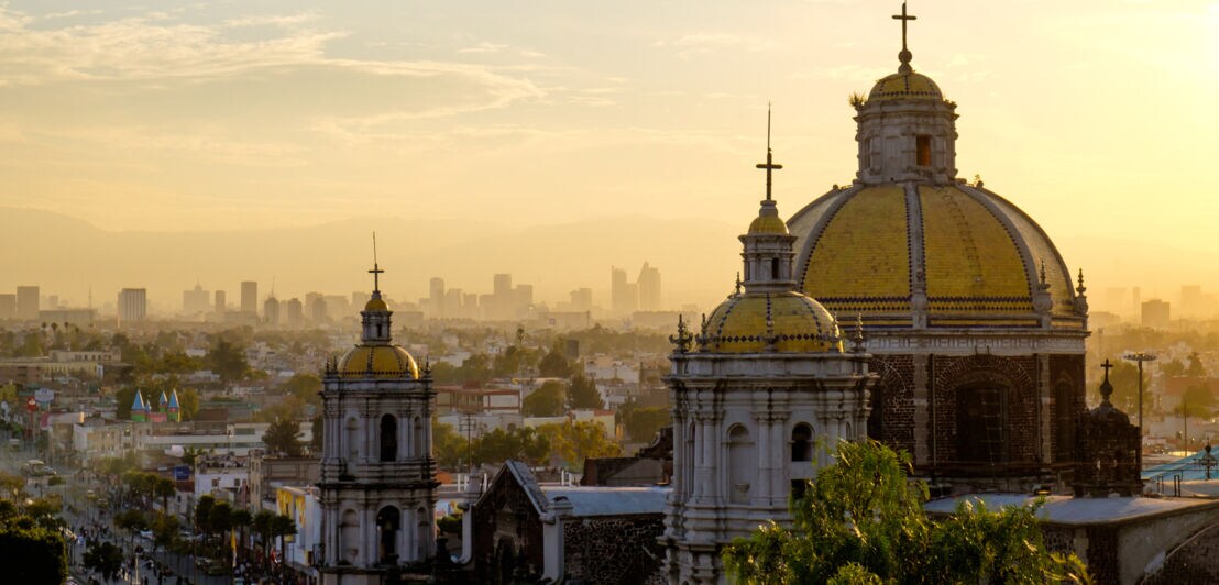Malerische Aussicht auf die Basilika von Guadalupe mit der Skyline von Mexiko-Stadt bei Sonnenuntergang