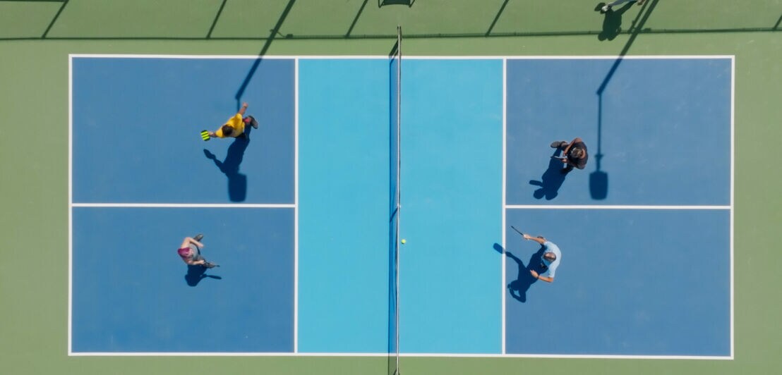 Top-Down-Aufnahme von vier Personen auf einem Tennisplatz, die Pickleball als Doppel spielen