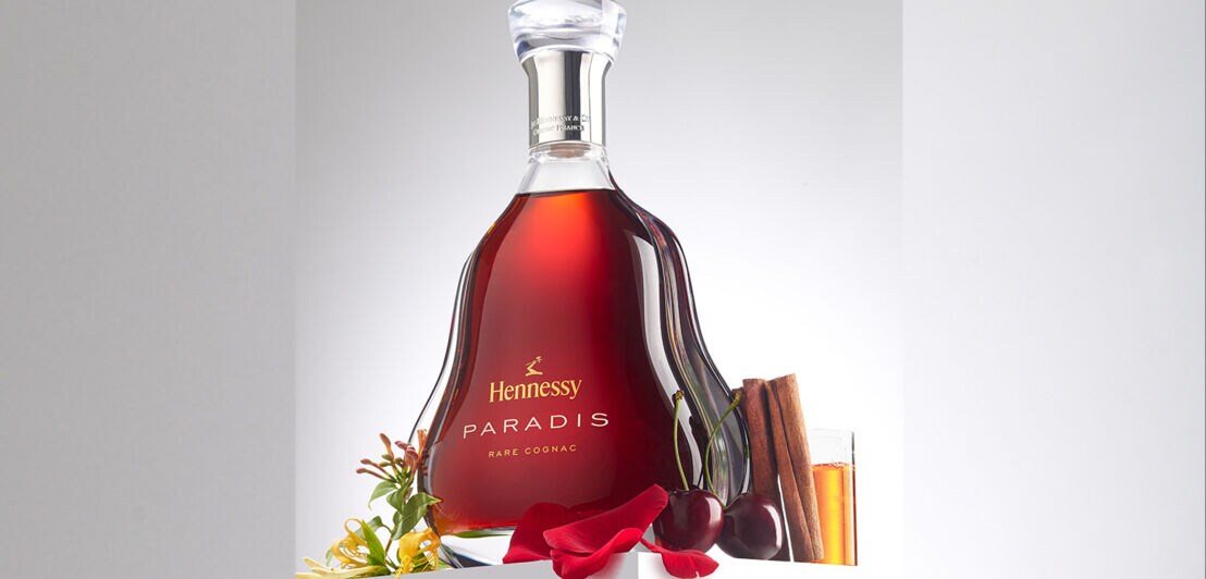 Eine Flasche Hennessy Paradise umgeben von Kirschen, Blütenblättern und Zimtstangen