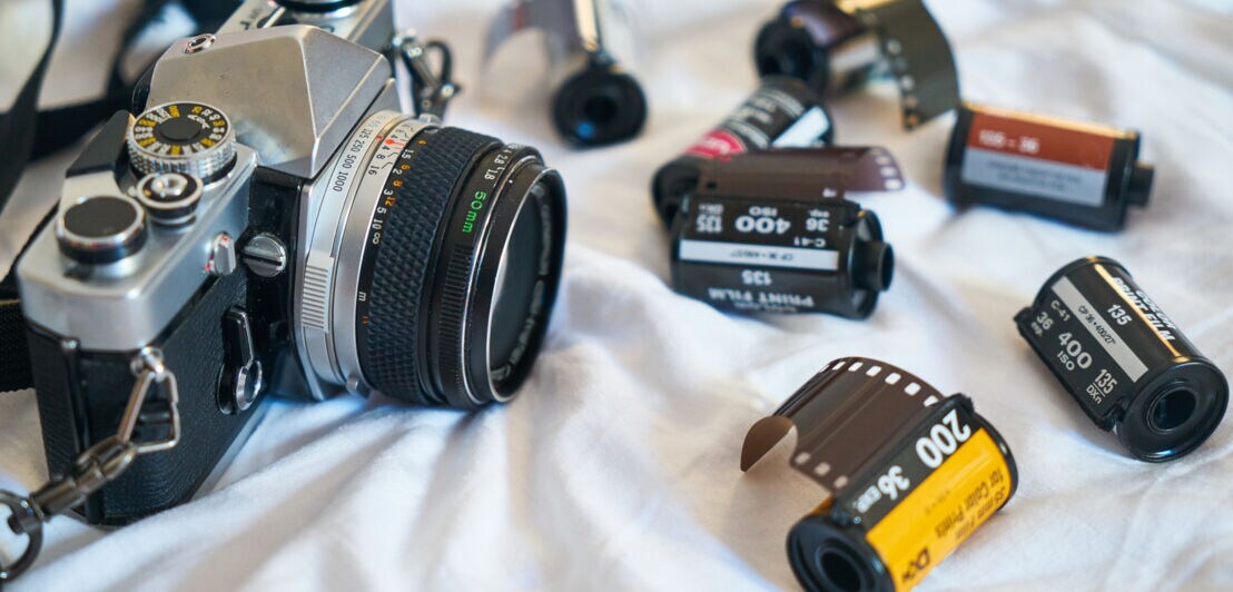 Eine analoge Kamera sowie mehrere Fotofilme liegen auf einem Stück Stoff
