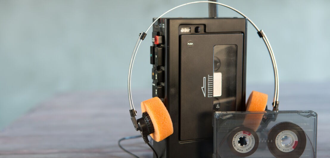 Ein Walkman samt Kopfhörern und einer Kassette vor unscharfem Hintergrund