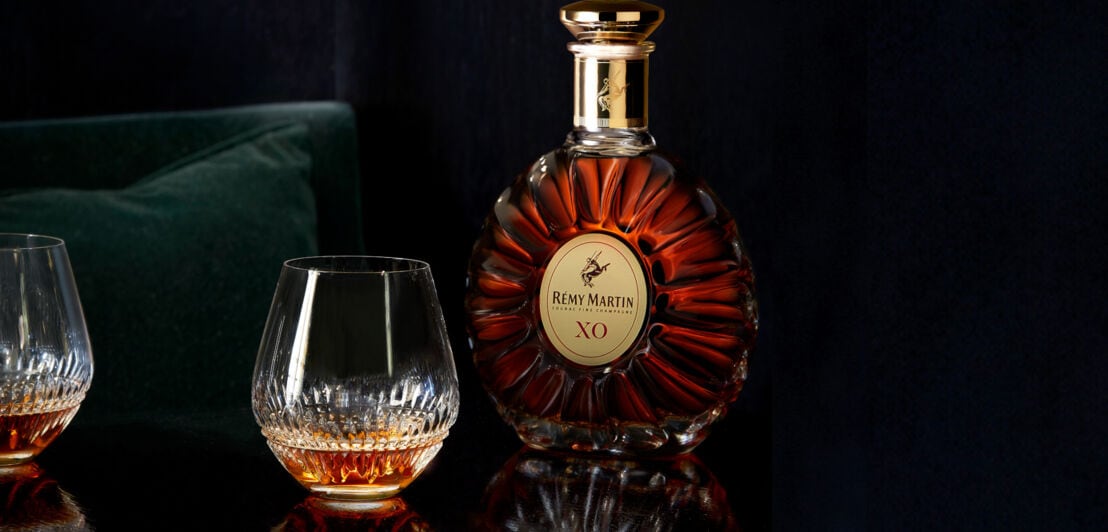 Eine Flasche Rémy Martin XO vor schwarzen Hintergrund, daneben ein gefülltes Cognac-Glas