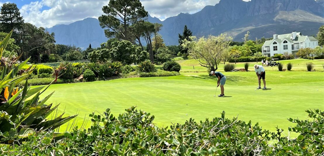 Zwei Personen spielen auf einer gepflegten Grünanlage Golf.