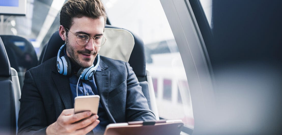 Ein Geschäftsmann sitzt mit Smartphone und Tablet im Zug