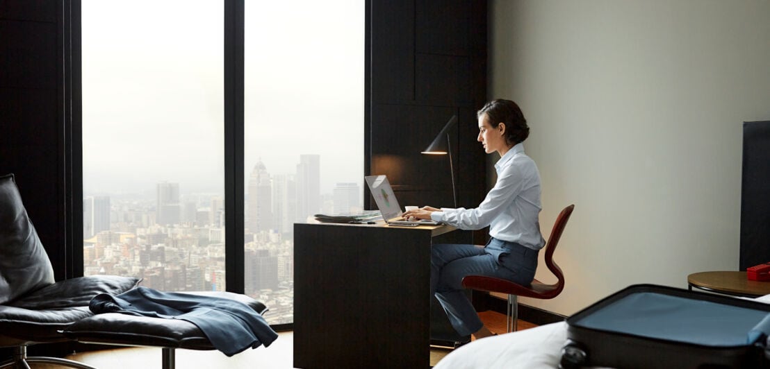 Eine Geschäftsfrau arbeitet in einem Hotelzimmer an einem Schreibtisch an ihrem Laptop