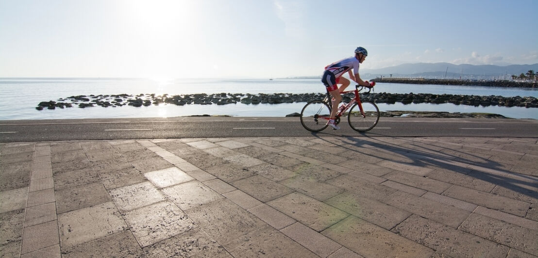 Mann auf Rennrad an Mallorcas Küste, im Vordergrund Pflaster