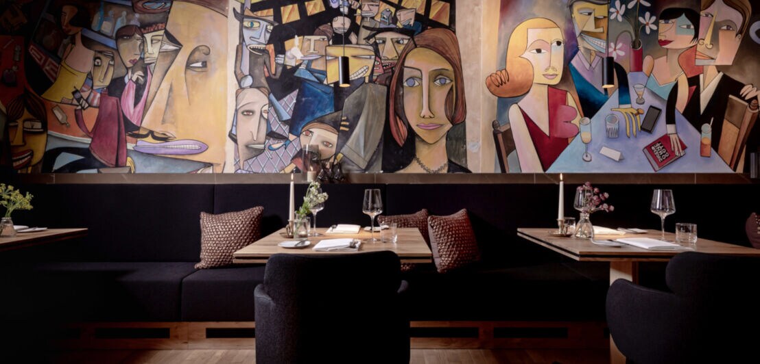 Tische und Bänke mit Kissen in einem Restaurant, an der Wand Malerei