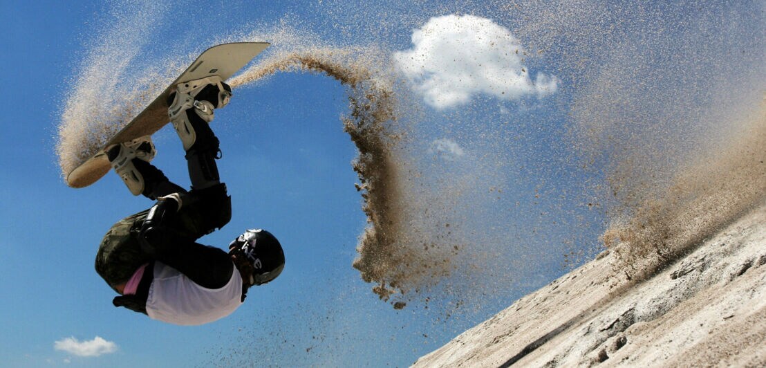 Eine Sandboarderin schlägt einen Salto auf der Sandpiste