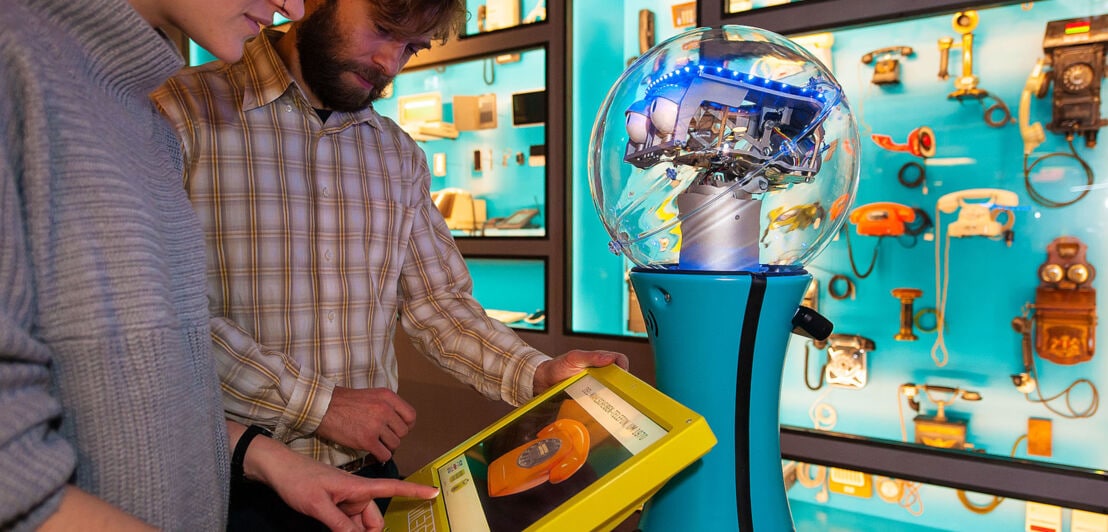 Zwei Personen schauen auf das Display eines Serviceroboters in einer Museumsausstellung