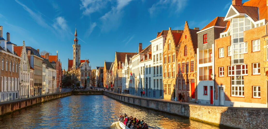 Ein Ausflugsboot mit Touristen fährt auf einem Wasserkanal durch die historische Altstadt von Brügge.