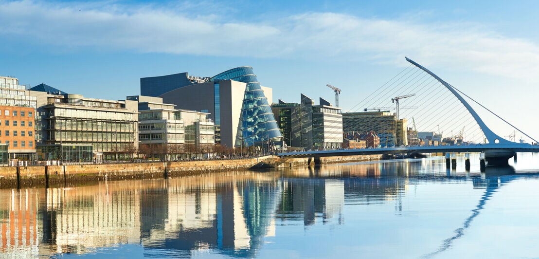 Moderne Gebäude sowie die Harfenbrücke über den Liffey River in Dublin an einem hellen, sonnigen Tag 