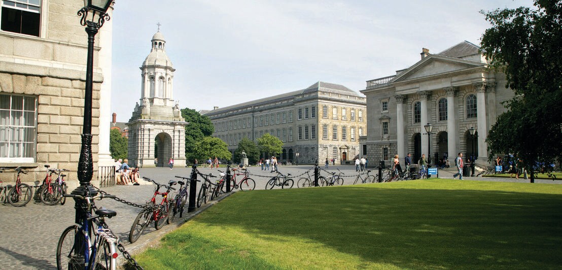 Das Trinity College mit einer Grünanlage im Vordergrund und mehreren abgestellten Fahrrädern